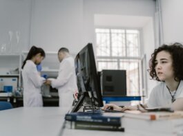 Focused woman working on a computer in a busy laboratory setting, showcasing teamwork and scientific research.