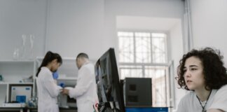 Focused woman working on a computer in a busy laboratory setting, showcasing teamwork and scientific research.