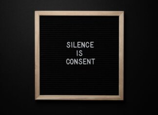 From above blackboard with written phrase SILENCE IS CONSENT on center on black background