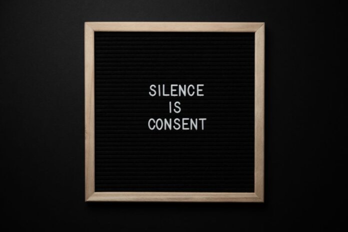 From above blackboard with written phrase SILENCE IS CONSENT on center on black background From above blackboard with written phrase SILENCE IS CONSENT on center on black background