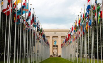 From below of various flags on flagpoles located in green park in front of entrance to the UN headquarters in Geneva