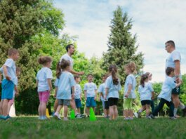 Group of children and teachers playing and learning in a sunny park setting.