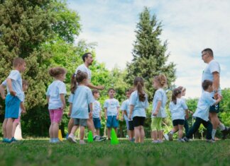 Group of children and teachers playing and learning in a sunny park setting.