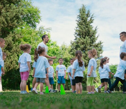 Group of children and teachers playing and learning in a sunny park setting.