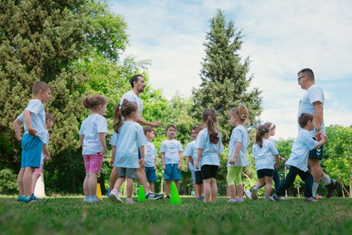 Group of children and teachers playing and learning in a sunny park setting. Group of children and teachers playing and learning in a sunny park setting.