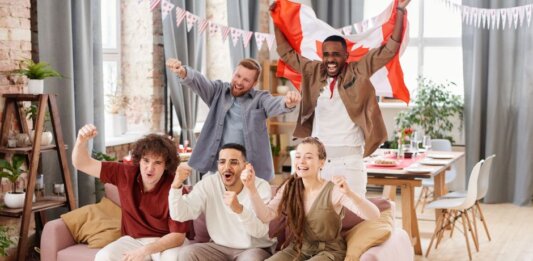 Group of friends cheering indoors with a Canadian flag, enjoying a lively moment together.