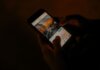 Hands holding a smartphone browsing social media in low light.