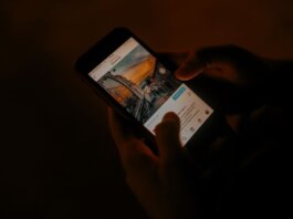 Hands holding a smartphone browsing social media in low light.
