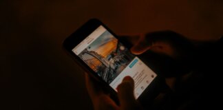 Hands holding a smartphone browsing social media in low light.