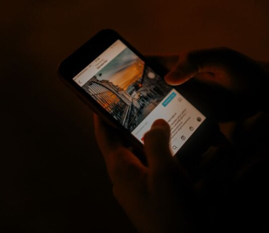 Hands holding a smartphone browsing social media in low light.