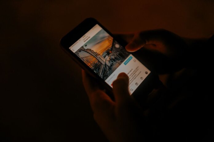 Hands holding a smartphone browsing social media in low light.