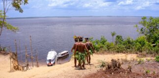 Indigenous men in traditional attire overlooking boats on the Amazon River.