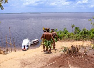 Береговая охрана выделила $1,6 млн коренным общинам на лодки Indigenous men in traditional attire overlooking boats on the Amazon River.