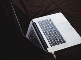 Modern laptop with backlit keyboard on a dark fabric surface, connected to a charger.