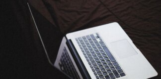 Modern laptop with backlit keyboard on a dark fabric surface, connected to a charger.