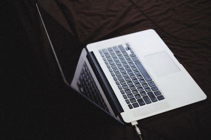 Modern laptop with backlit keyboard on a dark fabric surface, connected to a charger. Modern laptop with backlit keyboard on a dark fabric surface, connected to a charger.