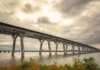 Консерваторы требуют раскрыть условия сделки по мосту Горди Хау Modern suspension bridge over water under dramatic cloudy skies, showcasing architectural feats.