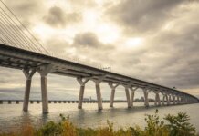 Modern suspension bridge over water under dramatic cloudy skies, showcasing architectural feats.