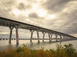 Modern suspension bridge over water under dramatic cloudy skies, showcasing architectural feats.