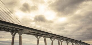 Modern suspension bridge over water under dramatic cloudy skies, showcasing architectural feats.