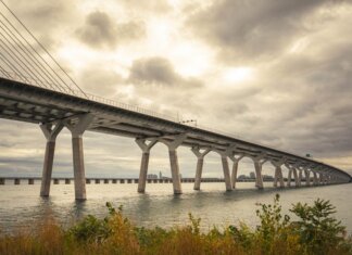 Modern suspension bridge over water under dramatic cloudy skies, showcasing architectural feats.