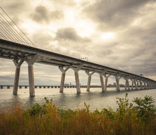 Modern suspension bridge over water under dramatic cloudy skies, showcasing architectural feats.