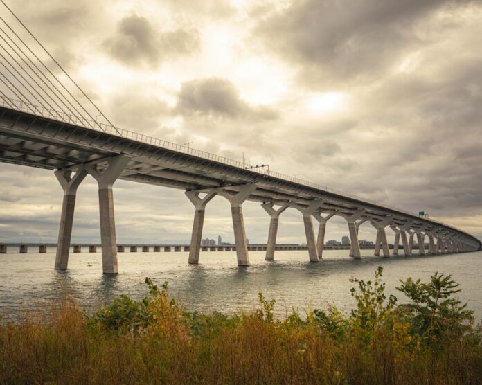 Modern suspension bridge over water under dramatic cloudy skies, showcasing architectural feats. Modern suspension bridge over water under dramatic cloudy skies, showcasing architectural feats.