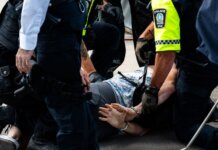 В Ошаве 13-летний подросток пытался ударить ножом сверстника Multiple police officers detain a person on a city street, using handcuffs to restrain them.