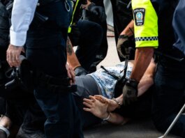 Multiple police officers detain a person on a city street, using handcuffs to restrain them.