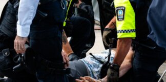 Multiple police officers detain a person on a city street, using handcuffs to restrain them.