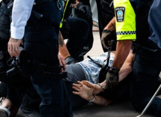 Multiple police officers detain a person on a city street, using handcuffs to restrain them.