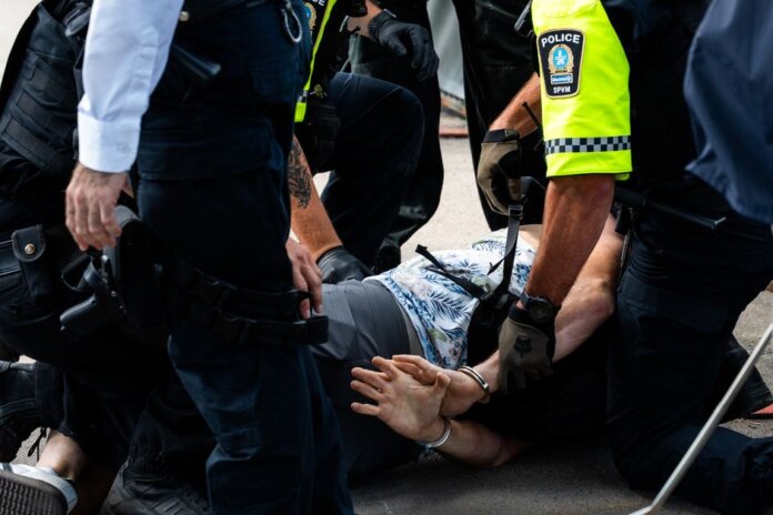 Multiple police officers detain a person on a city street, using handcuffs to restrain them. Multiple police officers detain a person on a city street, using handcuffs to restrain them.