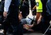 Multiple police officers detain a person on a city street, using handcuffs to restrain them.
