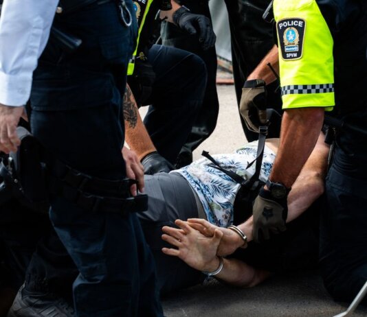 Multiple police officers detain a person on a city street, using handcuffs to restrain them.