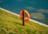 Как не утонуть в Великих озёрах: советы экспертов из Ватерлоо Orange lifebuoy hangs on a wooden post by a calm lake, symbolizing safety and preparedness.