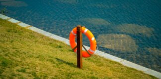Orange lifebuoy hangs on a wooden post by a calm lake, symbolizing safety and preparedness.