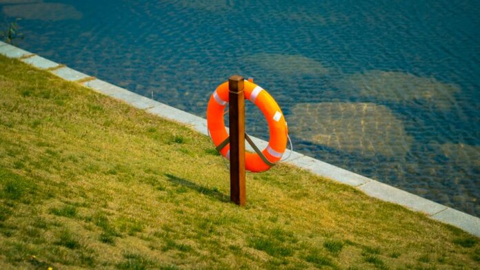 Orange lifebuoy hangs on a wooden post by a calm lake, symbolizing safety and preparedness.