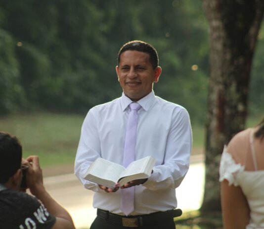 Pastor conducts a ceremony outdoors holding an open book with wedding participants.