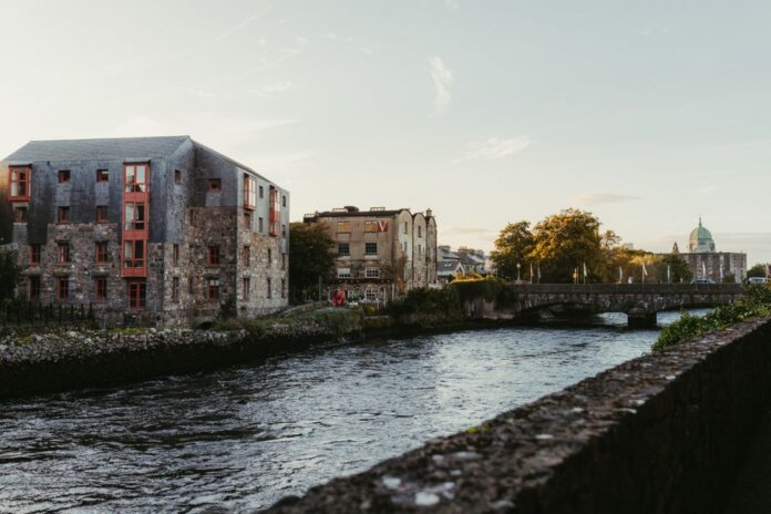 Picturesque view of the river in Galway, Ireland at sunset with historic buildings and a charming bridge. Picturesque view of the river in Galway, Ireland at sunset with historic buildings and a charming bridge.