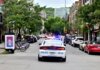 Police car driving through urban street lined with trees and parked bicycles.