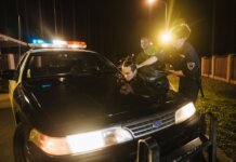 Police officers apprehending a suspect at night under streetlights by a patrol car.