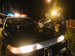 Police officers apprehending a suspect at night under streetlights by a patrol car.