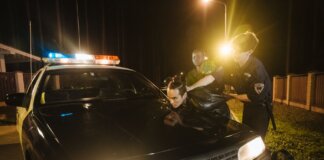 Police officers apprehending a suspect at night under streetlights by a patrol car.