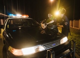 Police officers apprehending a suspect at night under streetlights by a patrol car.