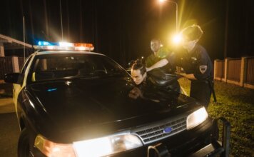 Женщина арестована за нападение с ножом в Ошаве Police officers apprehending a suspect at night under streetlights by a patrol car.