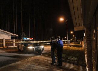 Мужчина обвиняется в нападении с мачете в Реджайне Police officers at a nighttime crime scene with a police car and caution tape under streetlights.