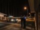 Police officers at a nighttime crime scene with a police car and caution tape under streetlights.
