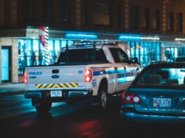 Police pickup with tail light riding on asphalt roadway near car along building with glass showcase in city on evening time