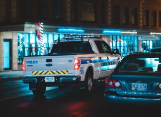 Police pickup with tail light riding on asphalt roadway near car along building with glass showcase in city on evening time
