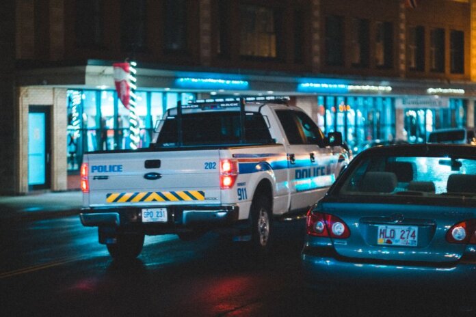 Police pickup with tail light riding on asphalt roadway near car along building with glass showcase in city on evening time Police pickup with tail light riding on asphalt roadway near car along building with glass showcase in city on evening time